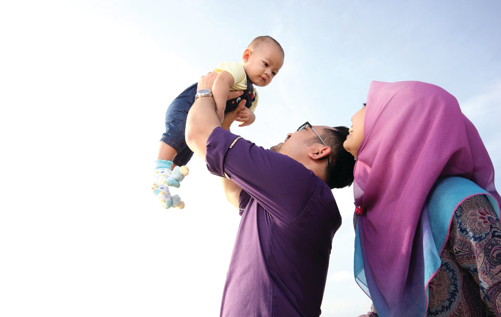 Asian parents lifting baby against blue sky