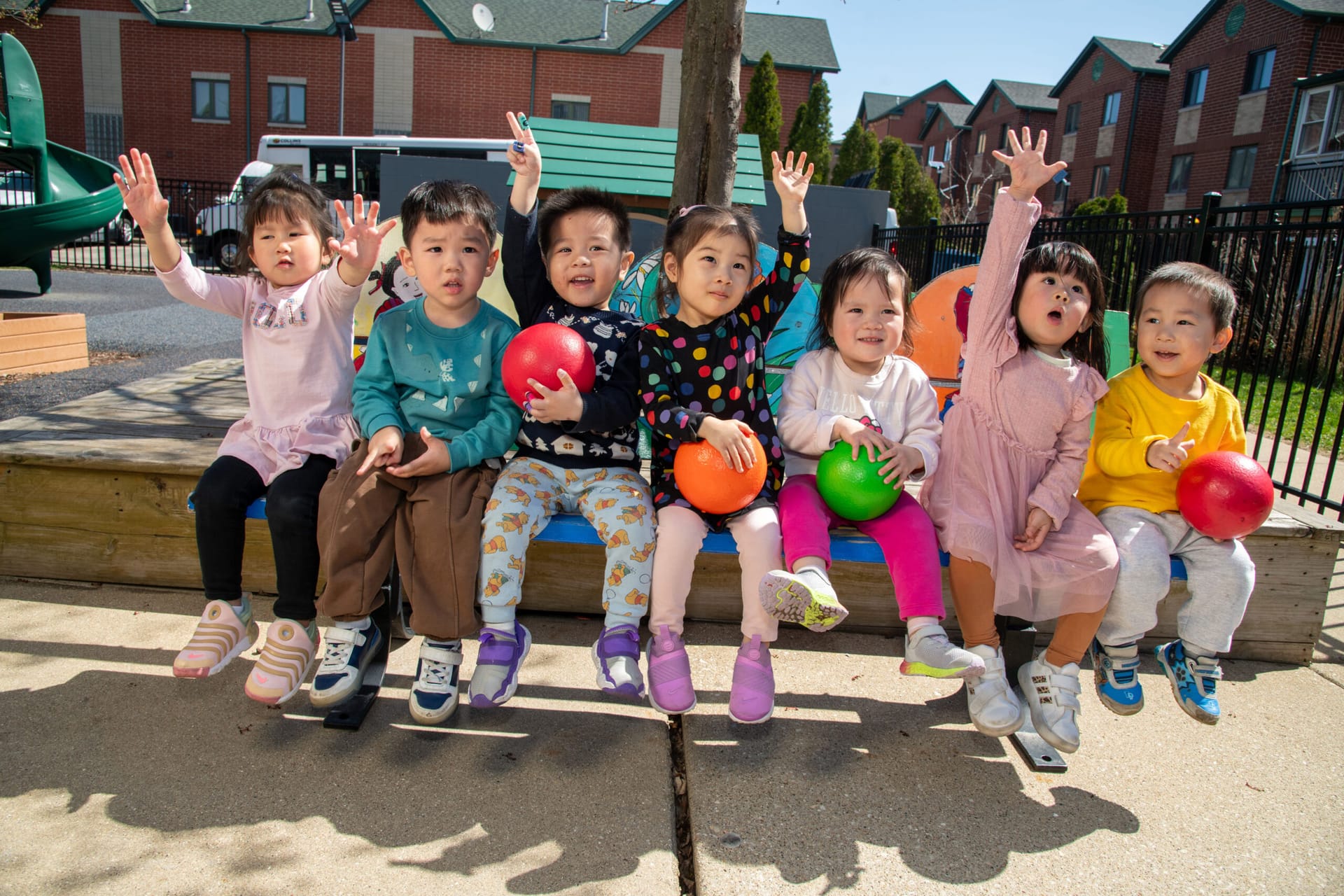 Seven pre-school children sitting on a bench outdoors